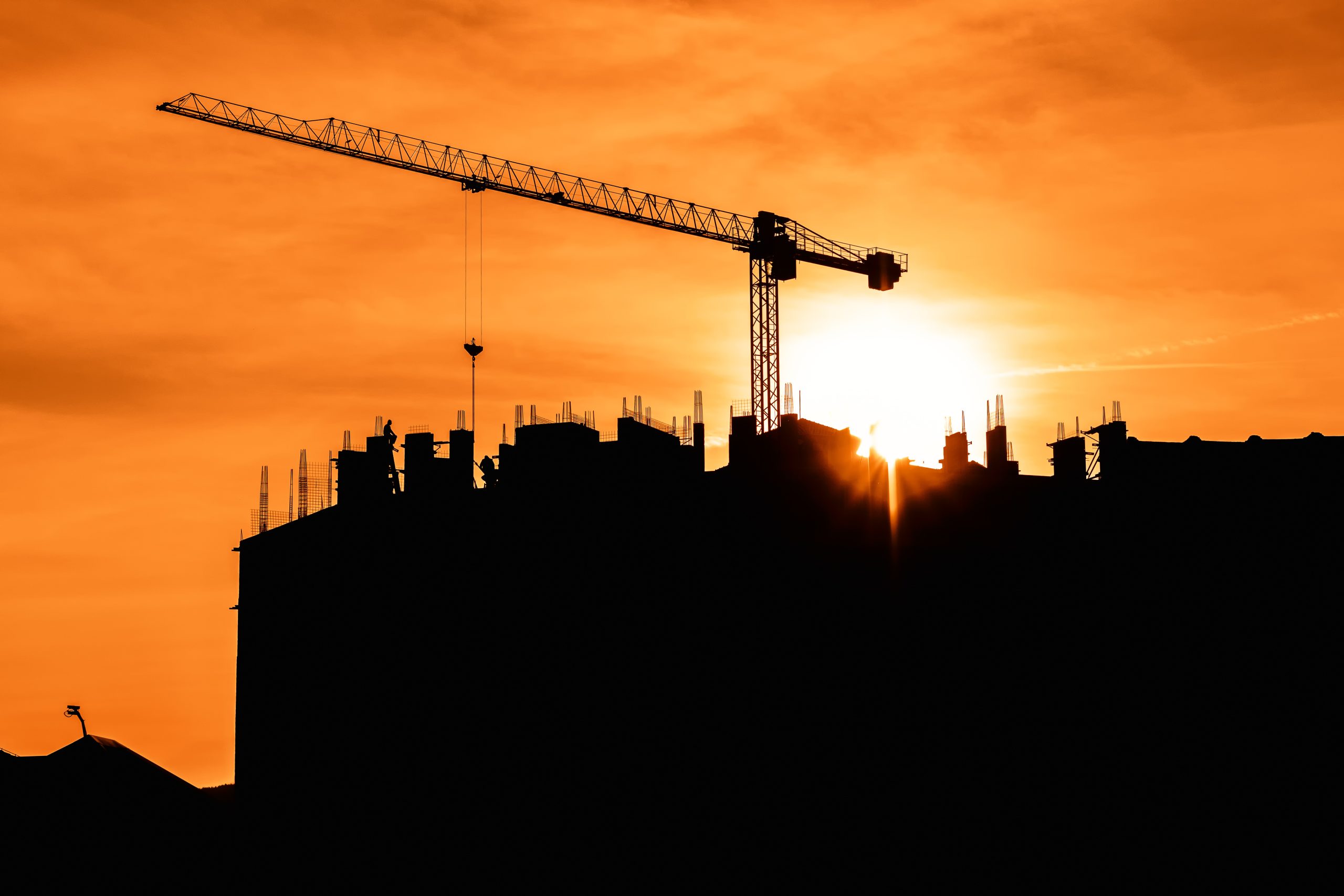 Construction crane on site, back lit by setting sun. Construction industry and architecture concept